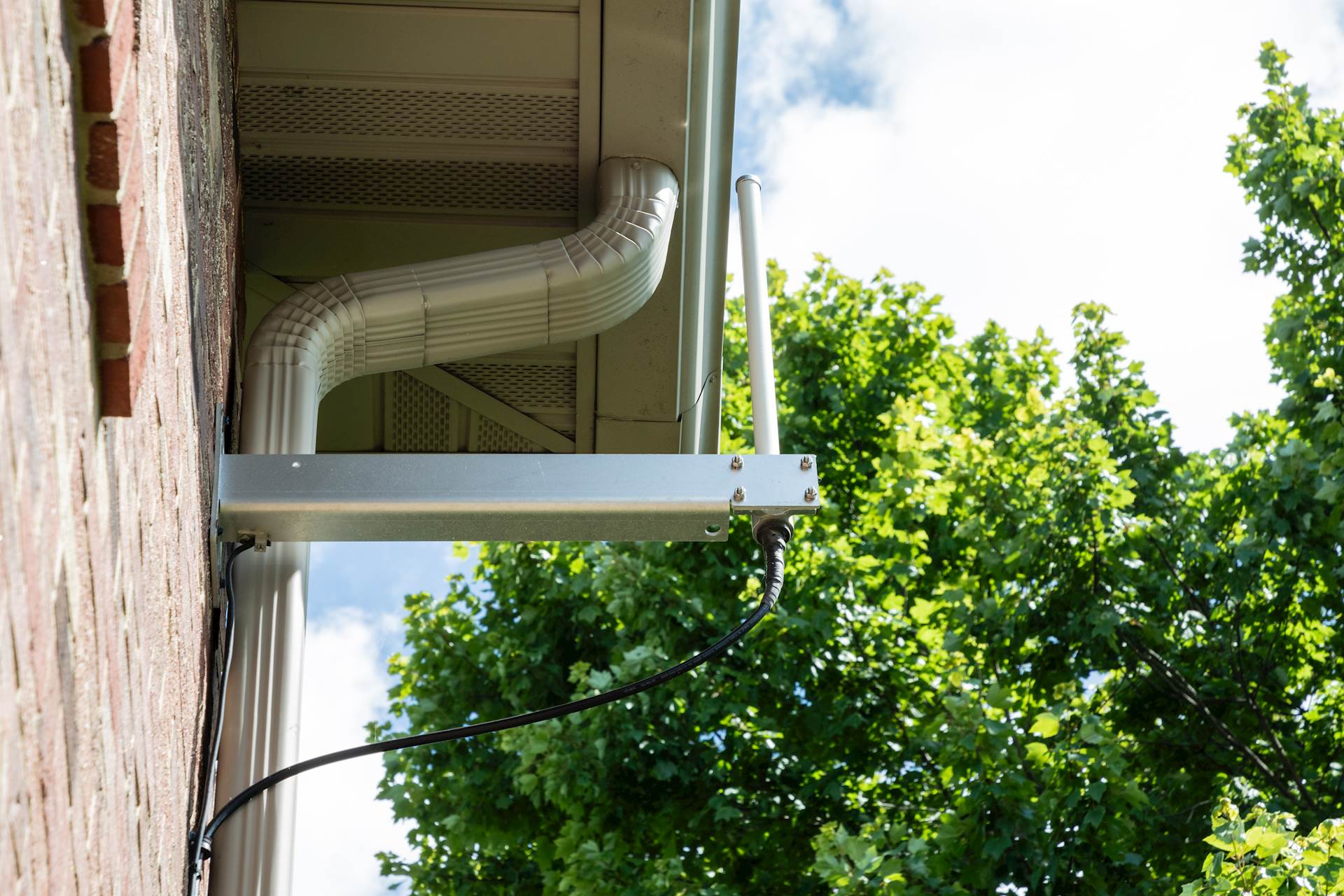 Close-up image of a device attached to the side of a brick house with a tree in the background