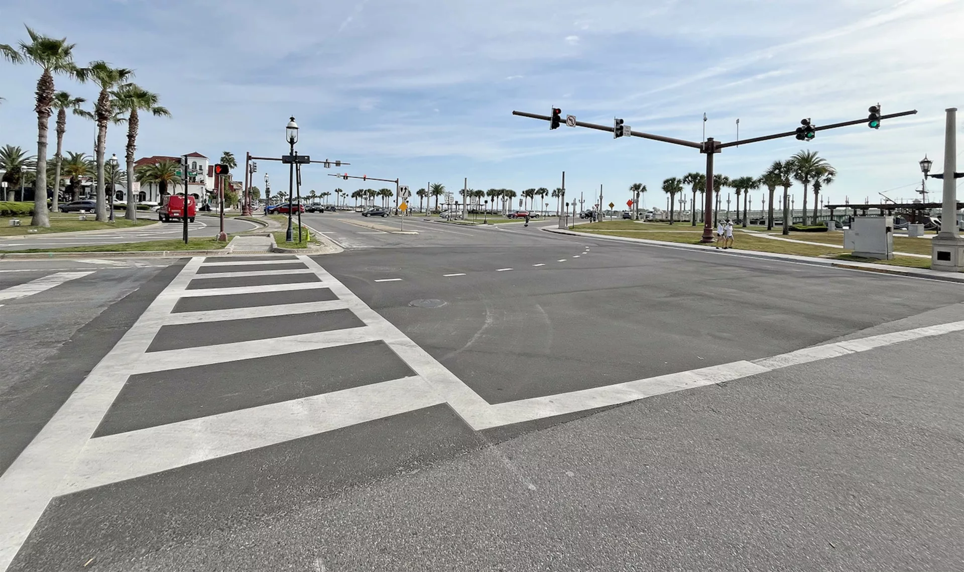 Stop lights; palm trees; walk way with white lines; blue sky with white clouds.